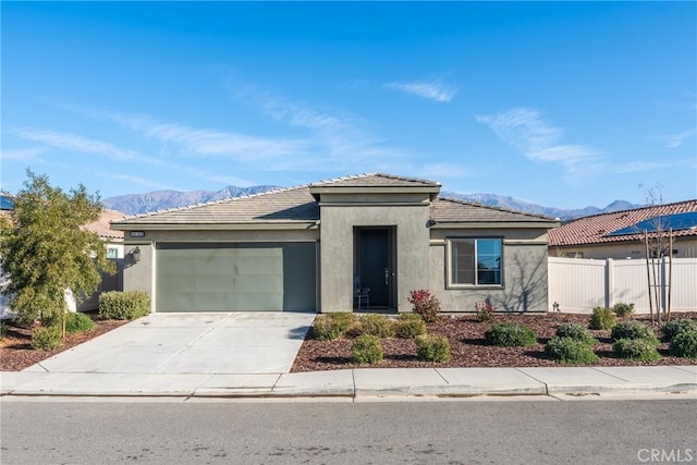 prairie-style home featuring driveway, an attached garage, fence, a mountain view, and stucco siding