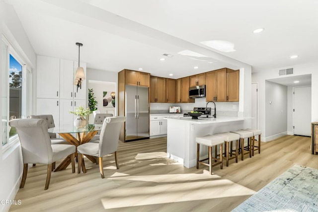 kitchen with pendant lighting, stainless steel appliances, a kitchen breakfast bar, kitchen peninsula, and light wood-type flooring