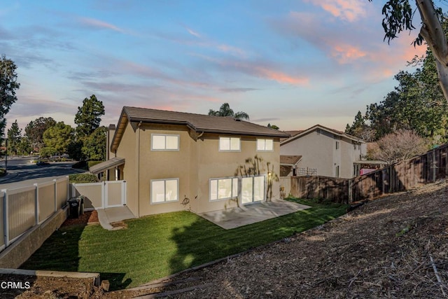 back house at dusk with a patio area and a yard