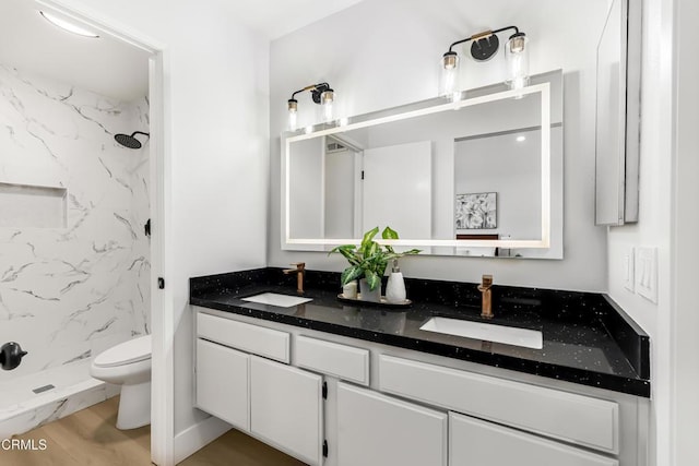 bathroom with wood-type flooring, toilet, vanity, and a tile shower