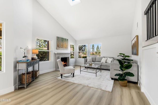 living room featuring high vaulted ceiling, light wood-type flooring, a skylight, and a fireplace