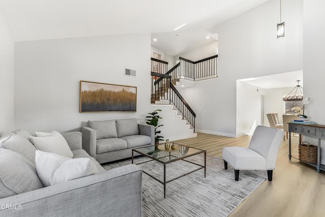 living room with a chandelier, light hardwood / wood-style floors, and a towering ceiling