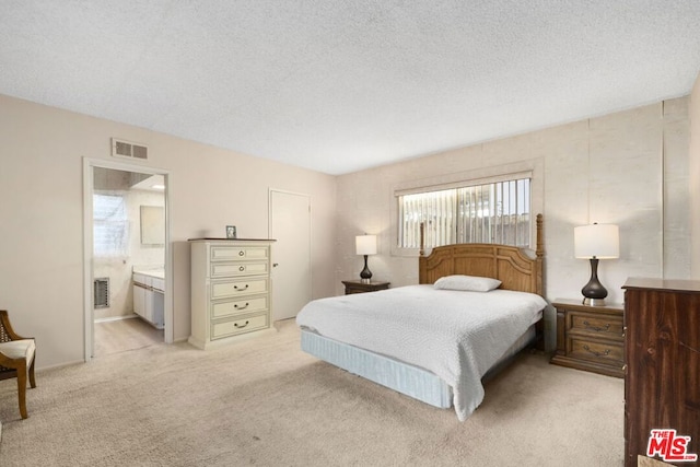 bedroom featuring a textured ceiling, light colored carpet, and ensuite bath