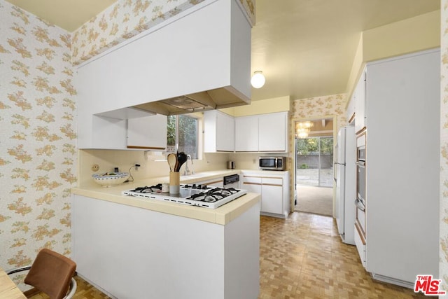 kitchen with kitchen peninsula, a healthy amount of sunlight, white cabinets, and white appliances