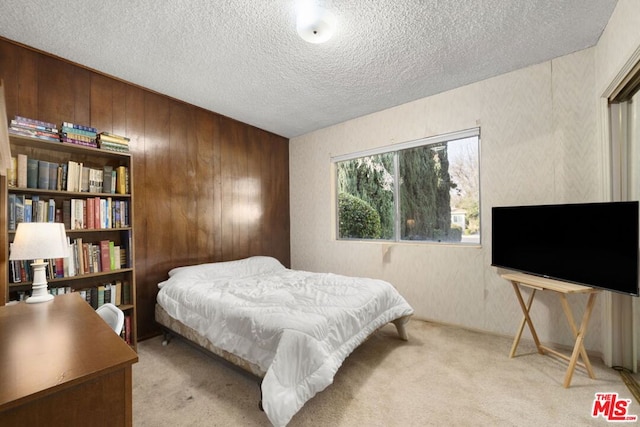 bedroom featuring a textured ceiling, light colored carpet, and wooden walls