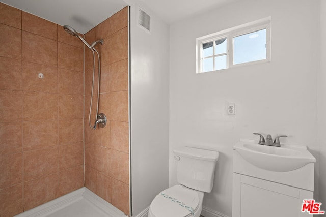 bathroom featuring toilet, vanity, and a tile shower