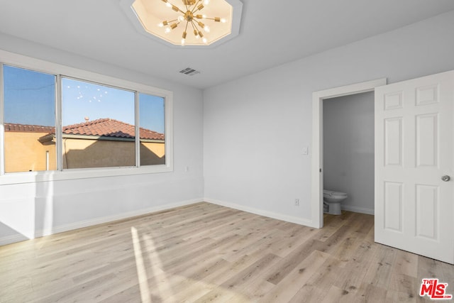 unfurnished bedroom featuring an inviting chandelier, ensuite bathroom, and light hardwood / wood-style floors