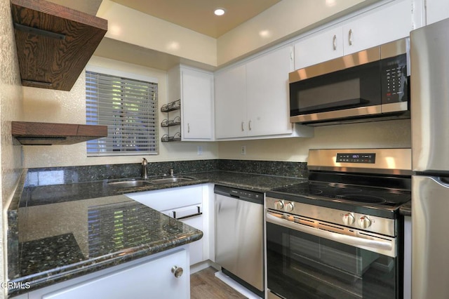 kitchen featuring white cabinetry, appliances with stainless steel finishes, wood-type flooring, dark stone counters, and sink