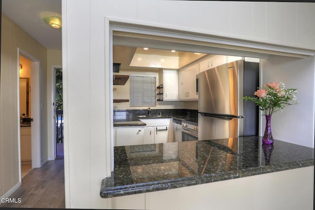 kitchen featuring dark hardwood / wood-style floors, kitchen peninsula, stainless steel refrigerator, white cabinetry, and dark stone counters