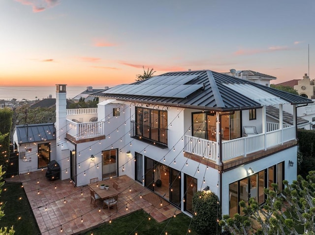 back house at dusk with a water view and a patio