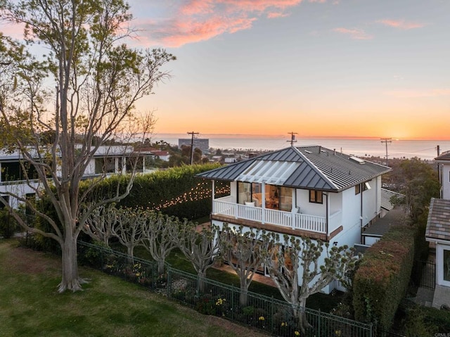 back house at dusk with a balcony, a lawn, and a water view