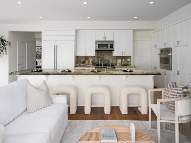 kitchen featuring white cabinets, a kitchen bar, stainless steel appliances, dark stone counters, and backsplash