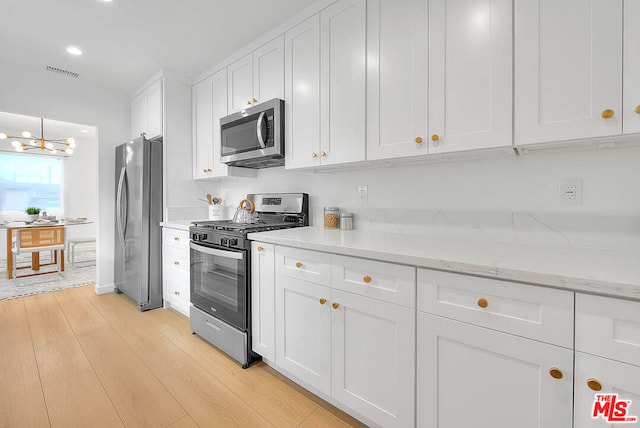 kitchen with stainless steel appliances, white cabinetry, light stone counters, and light wood-type flooring