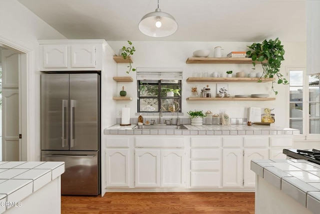 kitchen with tile countertops, stainless steel refrigerator, white cabinetry, sink, and hanging light fixtures