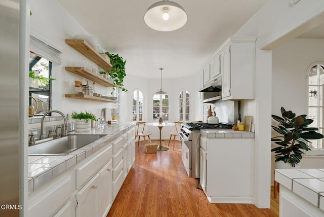 kitchen with sink, tile counters, stainless steel stove, and white cabinets