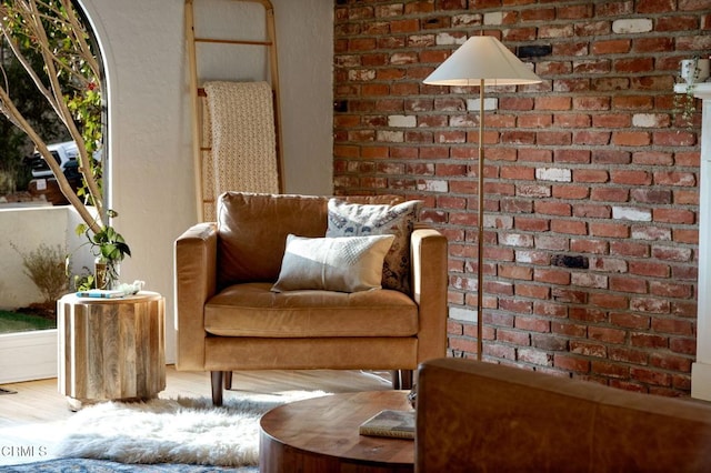 sitting room with brick wall and hardwood / wood-style floors