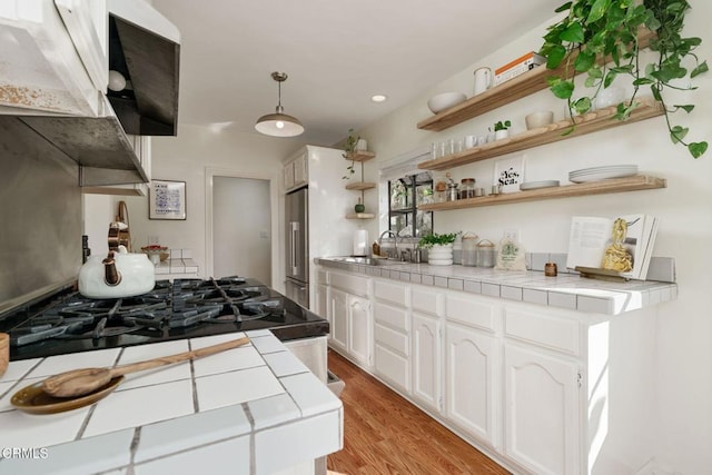 kitchen with high end refrigerator, tile countertops, light hardwood / wood-style flooring, hanging light fixtures, and white cabinets