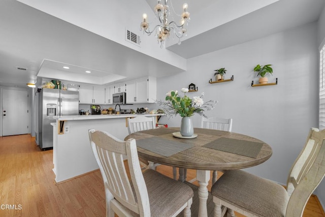 dining area with a raised ceiling, a notable chandelier, and light hardwood / wood-style floors