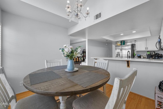 dining area featuring a raised ceiling, light wood-type flooring, and a notable chandelier