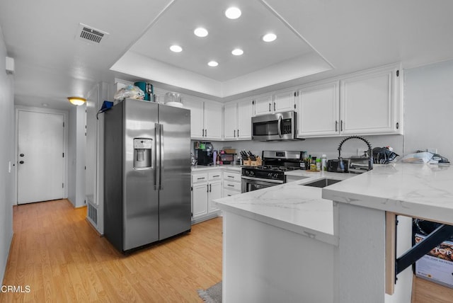 kitchen with light wood-type flooring, appliances with stainless steel finishes, white cabinetry, and a tray ceiling