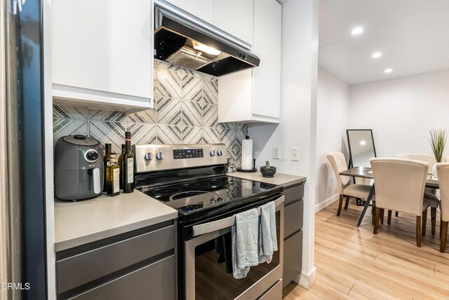 kitchen with stainless steel range with electric cooktop, ventilation hood, white cabinets, light hardwood / wood-style floors, and backsplash