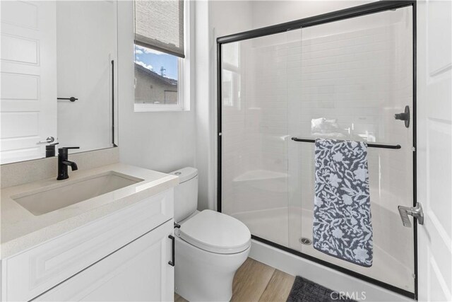 bathroom with vanity, hardwood / wood-style flooring, a shower with shower door, and toilet