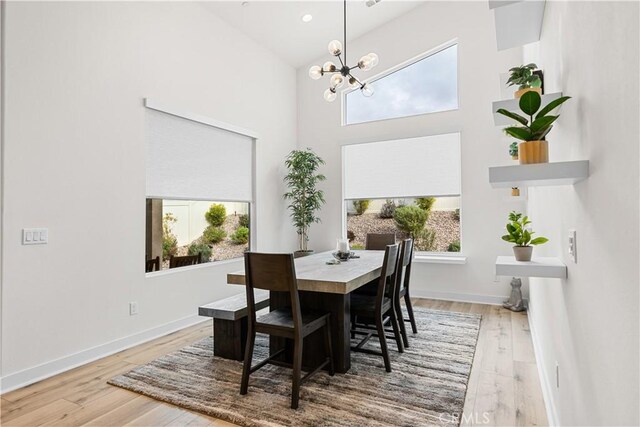 dining area featuring hardwood / wood-style flooring, a healthy amount of sunlight, an inviting chandelier, and high vaulted ceiling