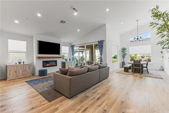 living room with high vaulted ceiling, an inviting chandelier, and light hardwood / wood-style flooring