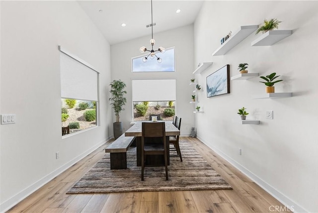 dining room with hardwood / wood-style flooring, a healthy amount of sunlight, a notable chandelier, and a towering ceiling