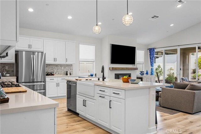 kitchen with white cabinetry, decorative light fixtures, a center island with sink, appliances with stainless steel finishes, and decorative backsplash