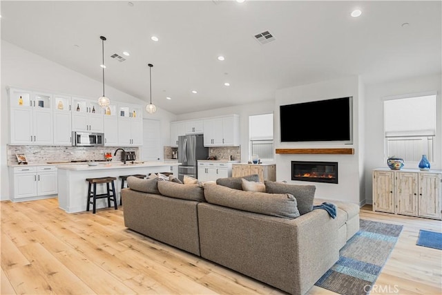 living room with lofted ceiling, sink, and light wood-type flooring