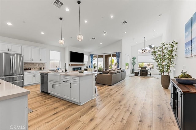 kitchen featuring stainless steel appliances, white cabinetry, tasteful backsplash, and a center island with sink