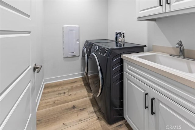 clothes washing area featuring sink, light hardwood / wood-style flooring, washing machine and dryer, and cabinets