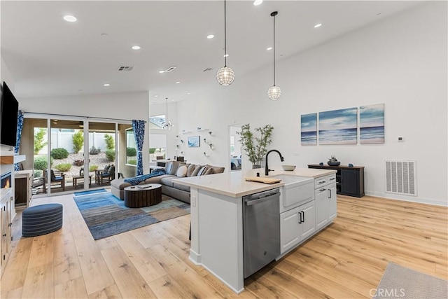 kitchen with decorative light fixtures, white cabinetry, stainless steel dishwasher, a center island with sink, and light hardwood / wood-style flooring