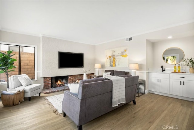 living room featuring light wood-type flooring, a brick fireplace, ornamental molding, and wet bar