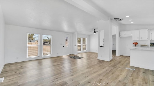 unfurnished living room with ceiling fan, vaulted ceiling with beams, and light wood-type flooring