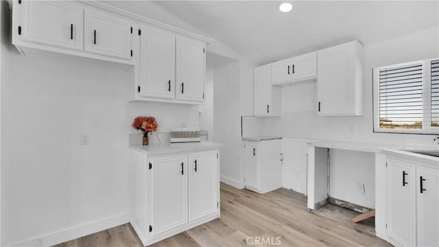 kitchen with vaulted ceiling, white cabinetry, and light hardwood / wood-style flooring