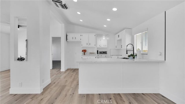 kitchen with light wood-type flooring, white cabinetry, sink, kitchen peninsula, and vaulted ceiling