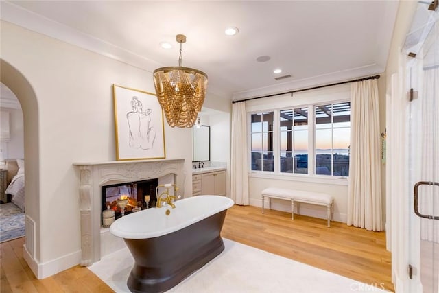 living area featuring a high end fireplace, sink, ornamental molding, a chandelier, and light wood-type flooring