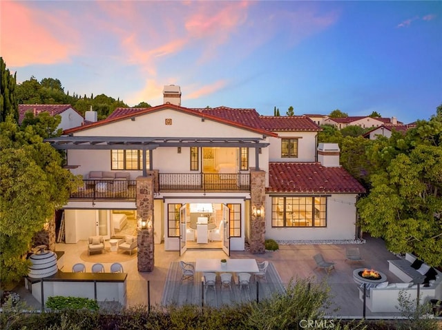 back house at dusk with an outdoor living space with a fire pit, a balcony, and a patio