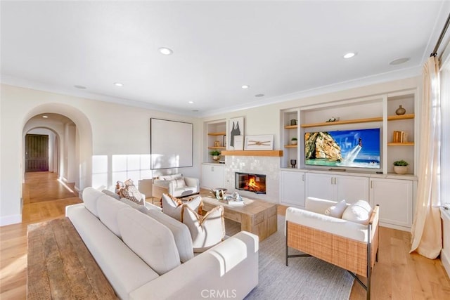 living room featuring a fireplace, ornamental molding, light hardwood / wood-style floors, and built in shelves