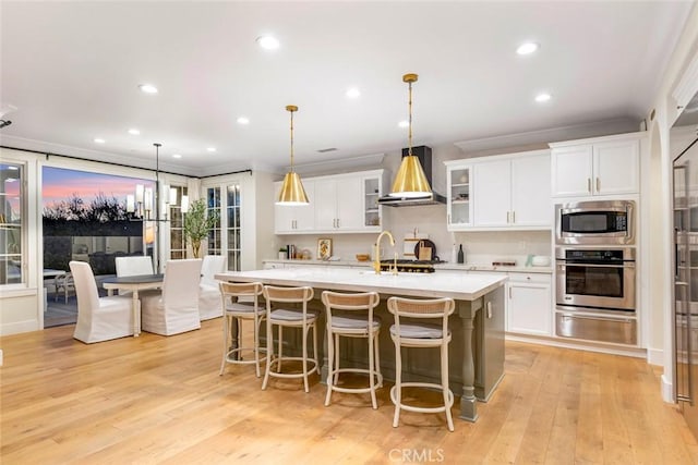 kitchen featuring white cabinets, appliances with stainless steel finishes, decorative light fixtures, a kitchen island with sink, and light hardwood / wood-style flooring