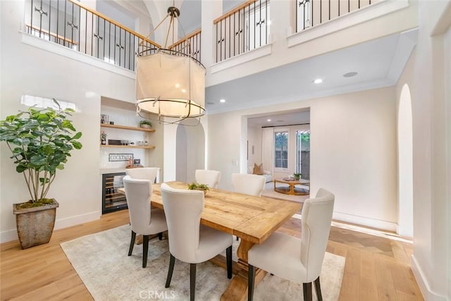 dining area with light hardwood / wood-style floors, a high ceiling, beverage cooler, and crown molding