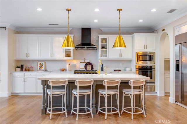 kitchen with wall chimney exhaust hood, a center island with sink, pendant lighting, and built in appliances