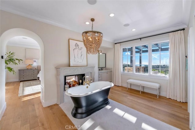 bathroom with a high end fireplace, hardwood / wood-style floors, a bathing tub, ornamental molding, and vanity