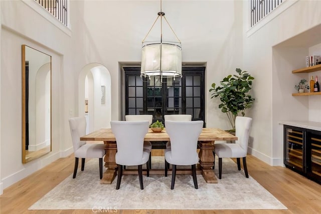 dining space with a high ceiling, a chandelier, wine cooler, and light hardwood / wood-style flooring