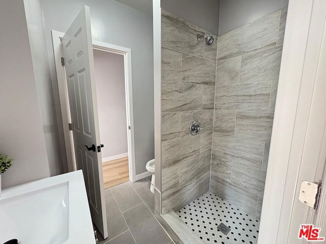 bathroom with tiled shower, toilet, and tile patterned flooring