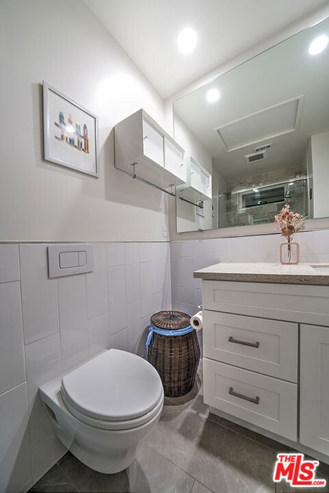 bathroom with toilet, vanity, tile walls, walk in shower, and tile patterned floors