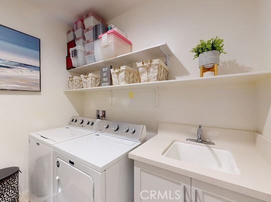 clothes washing area with sink, washer and dryer, and cabinets