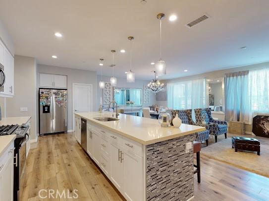 kitchen with white cabinetry, stainless steel appliances, a kitchen island with sink, hanging light fixtures, and sink